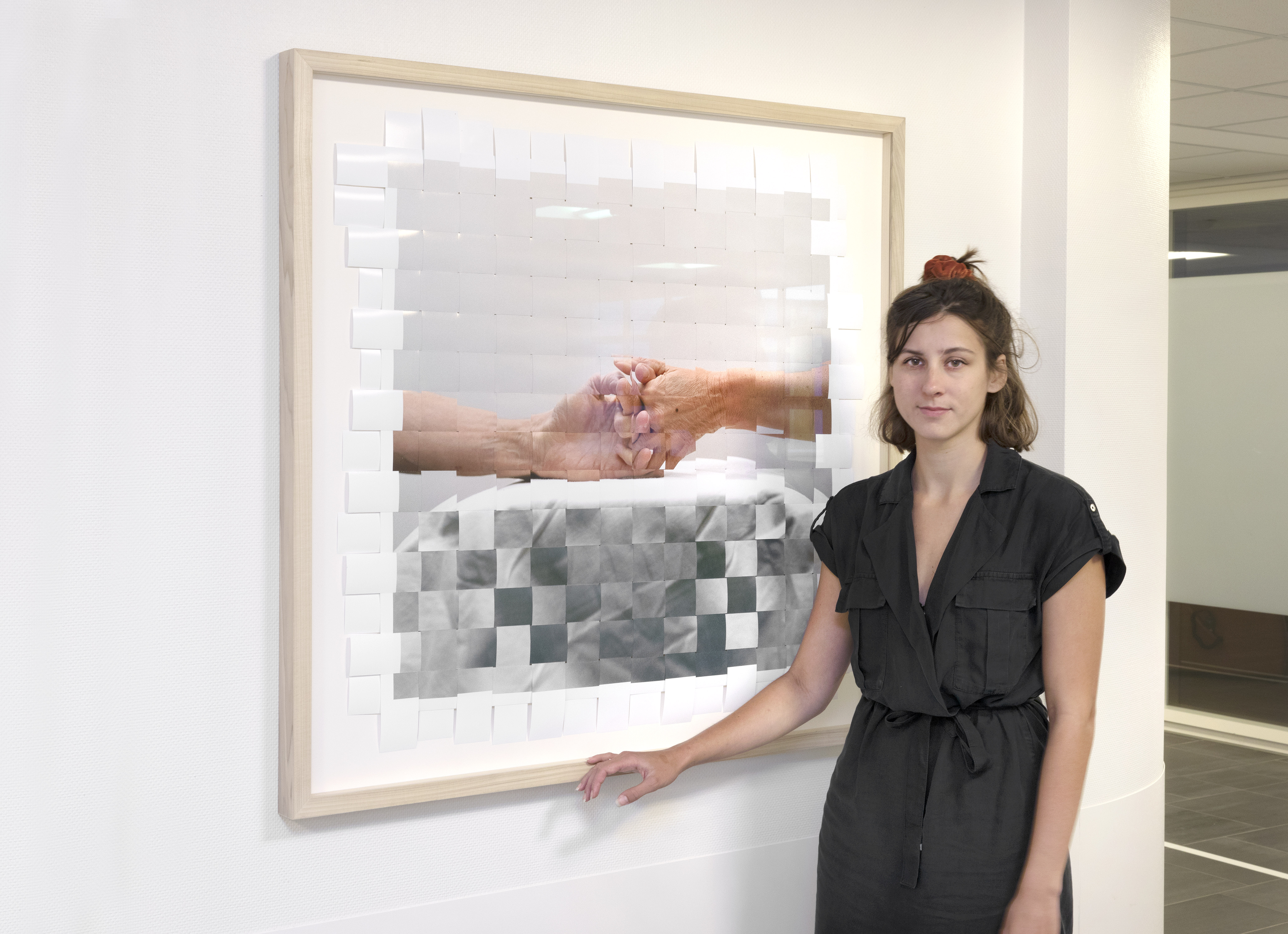 Laura van Erp poseert bij een van haar kunstwerken, een foto van twee handen die elkaar beetpakken