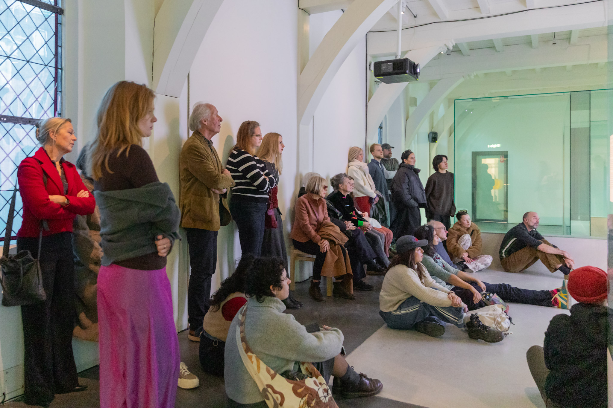 publiek bekijkt zittend op de grond en staand de documentairefilm in de expositiezaal