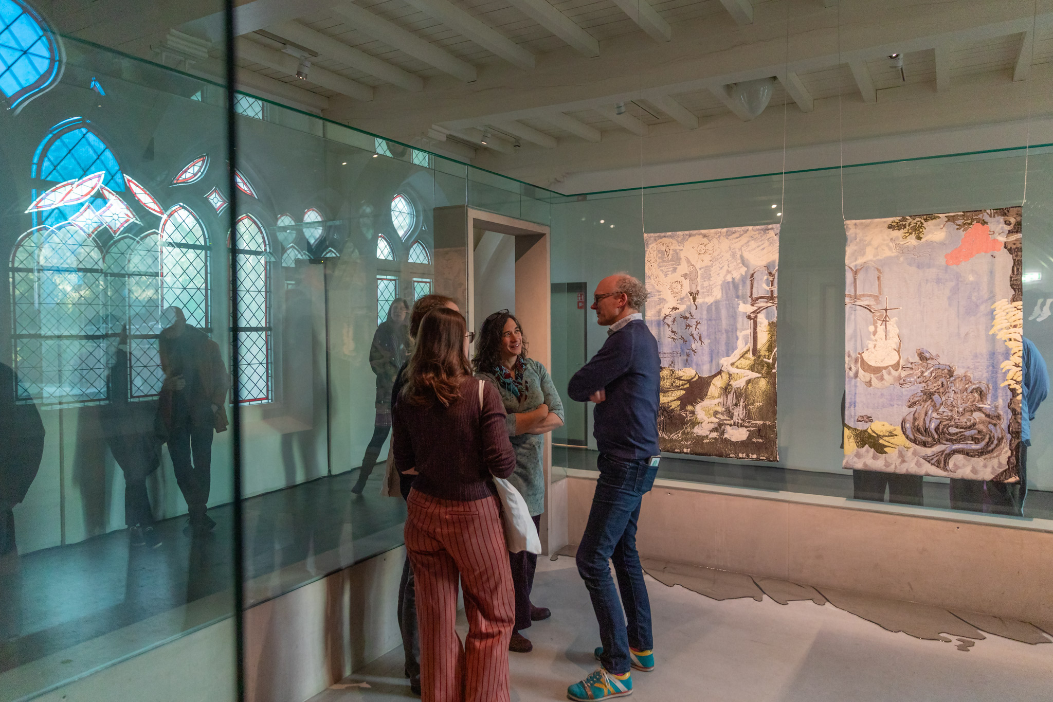 een groepje bezoekers staat met elkaar te praten met rechts in beeld de wandkleden in de expositie
