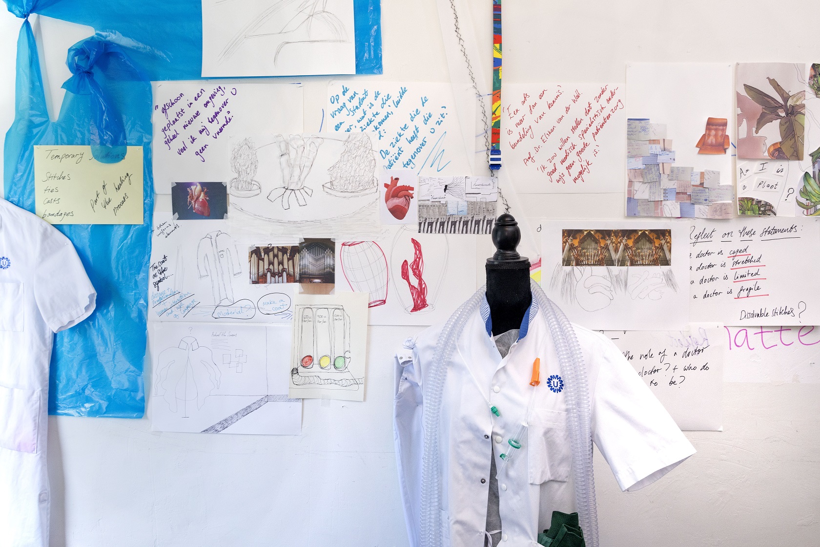 pop met doktersjas staat voor een collage met schetsen, teksten, kleuren en materialen op de wand in de studio van Sarah